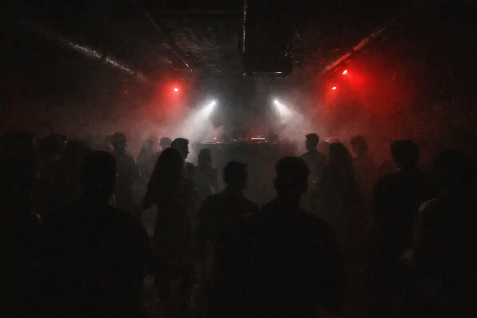 Underground techno club with strobe lights and dancers, DJ booth glowing in the distance